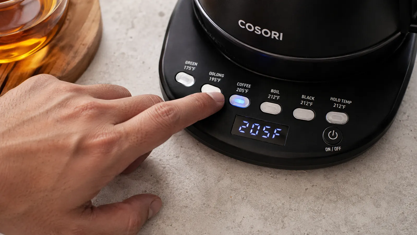 Hand pressing a temperature preset button on the Cosori electric kettle control panel